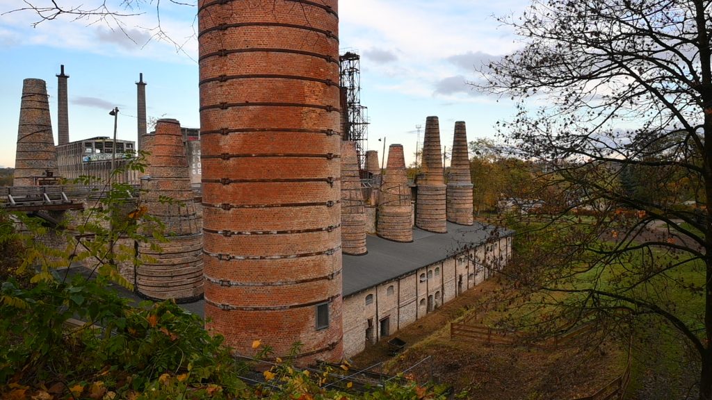 Man sieht große alte Industriegebäude mit hohen Schornsteinen und anderen Aufbauen aus Backstein. Sie gehören zum Museumspark Rüdersdorf.