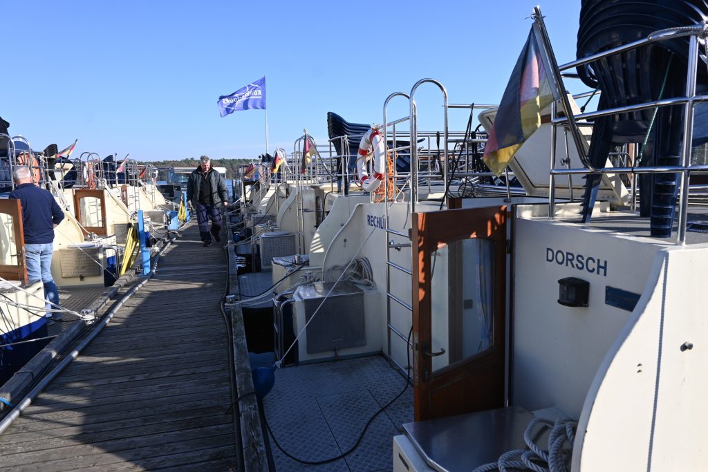 Man sieht einen Steg an dem viele ähnlich aussehende Hausboote der Kormoran-Baureihe festgemacht sind.